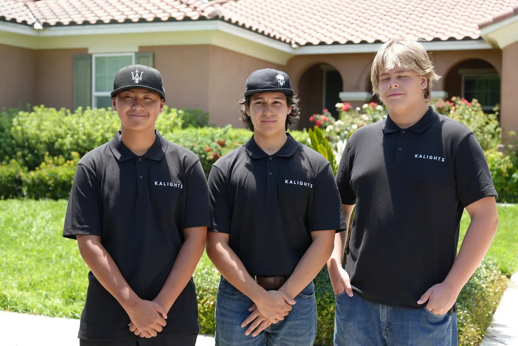 Three Kalights crew members in black company polos and caps standing together on a front walkway in daylight