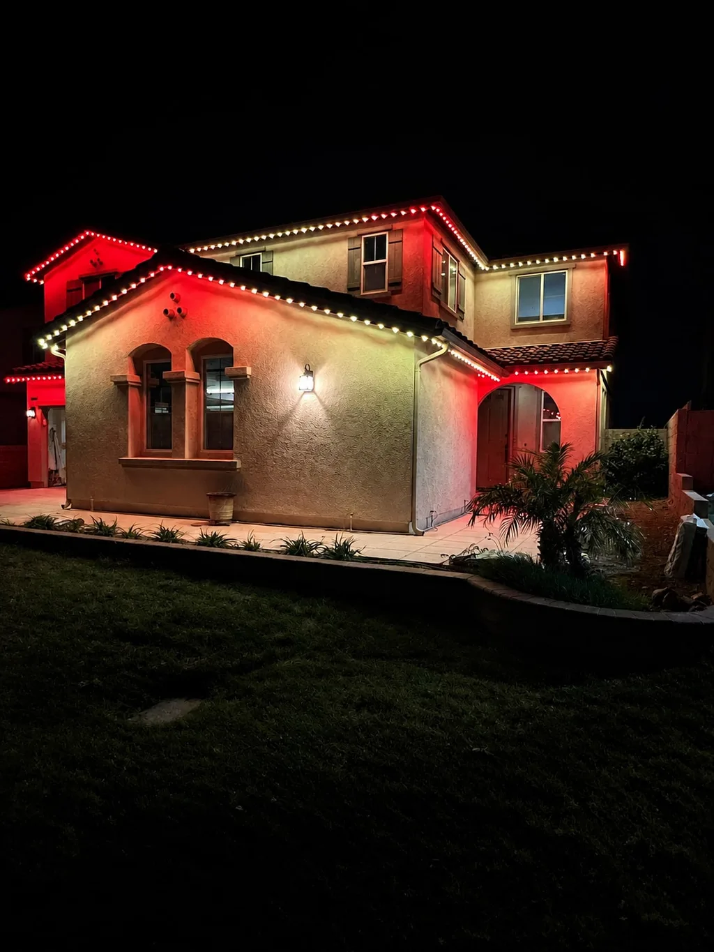 Rendering of a two-story house at night washed in red light with warm white lights along its rooflines